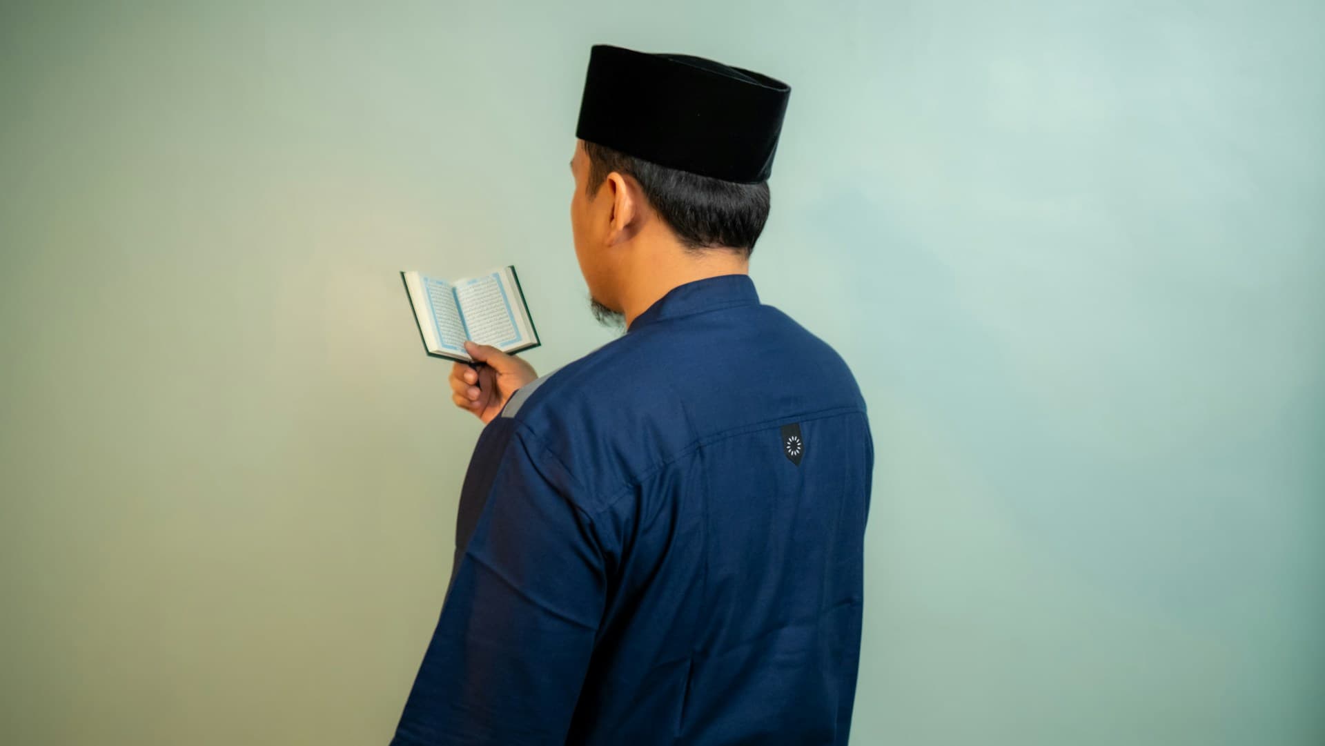 Seorang muslim berpeci membaca mushaf saku